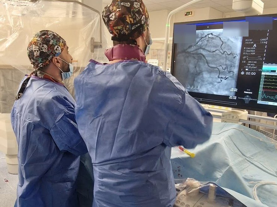 Deux praticiens analysent une coronarographie affichée à l'écran en salle de cathétérisme